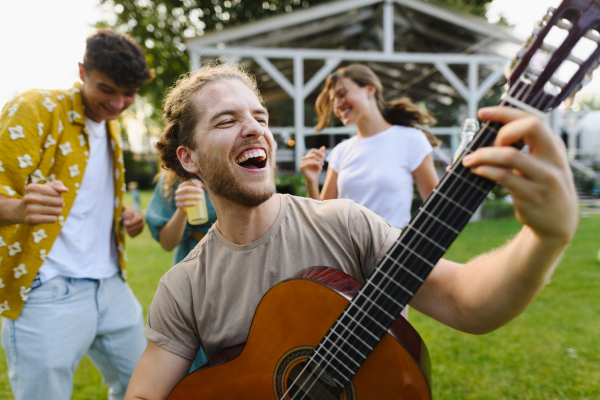 Handsome man playing at guitar at party. Friends and family talking and having fun at a summer grill garden party.