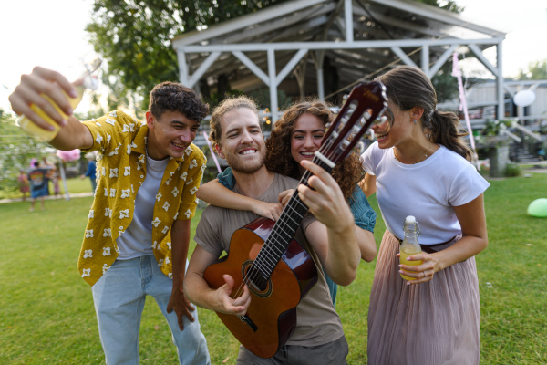 Handsome man playing at guitar for dancing friends at party. Friends and family dancing and having fun at a summer grill garden party.