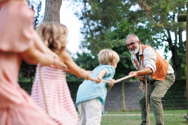 Grandfather has tug of war with their grandchildren. Fun games at family garden party.