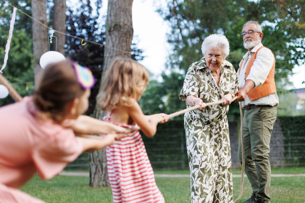 Grandparents have a tug of war with their granddaughters. Fun games at a family garden party.