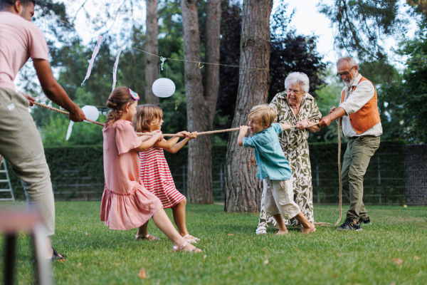 Grandparents have a tug of war with their grandchildren. Fun games at family garden party.