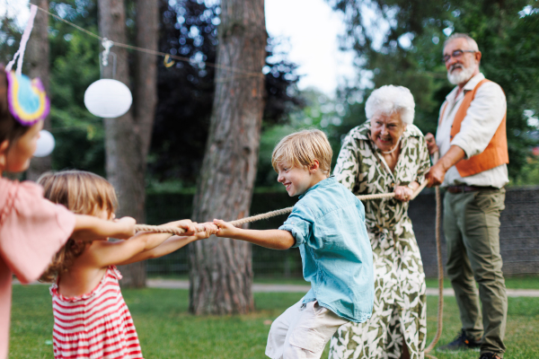 Grandparents have a tug of war with their grandchildren. Fun games at family garden party.