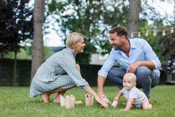 Young family with a baby playing in grass at family garden party. Father, mother, and a small child at birthday party.