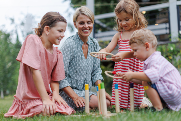 Woman playing with three kids in the garden, outdoor garden games, sitting on grass.