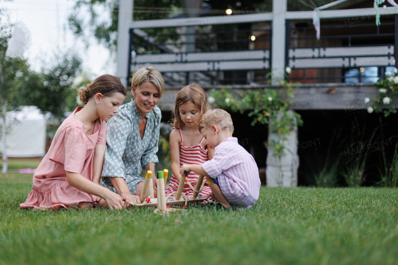 Woman playing with three kids in the garden, outdoor garden games, sitting on grass.