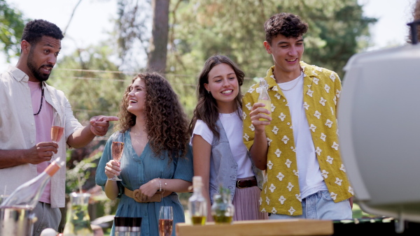 Friends and family talking and having fun at a summer grill garden party. People at the party laughing, holding glasses with drinks.