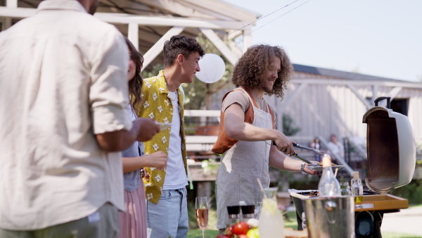 Friends and family talking and having fun at a summer grill garden party. People at the party laughing, holding glasses with drinks.