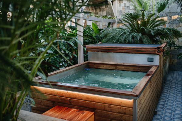 Wooden hot tub among the greenery, houseplants, in the hotel greenhouse. Wellness weekend in spa.