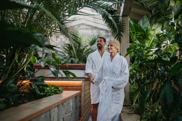 Beautiful couple standing by hot tub, wearing bathrobes, enjoying romantic wellness weekend in the spa. Concept of Valentine's Day.