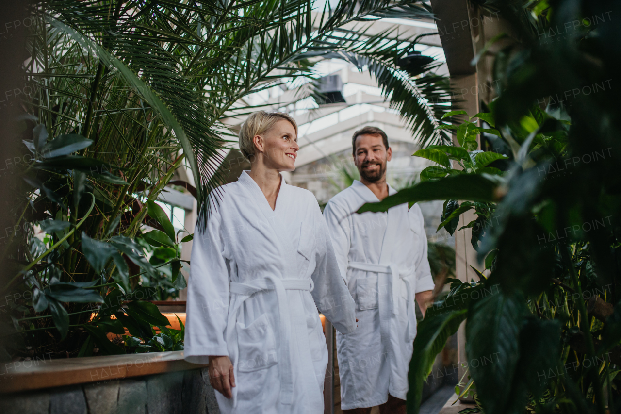 Beautiful couple in spa robes standing in hotel greenhouse, looking at each another, enjoying romantic wellness weekend in the spa. Concept of Valentine's Day.