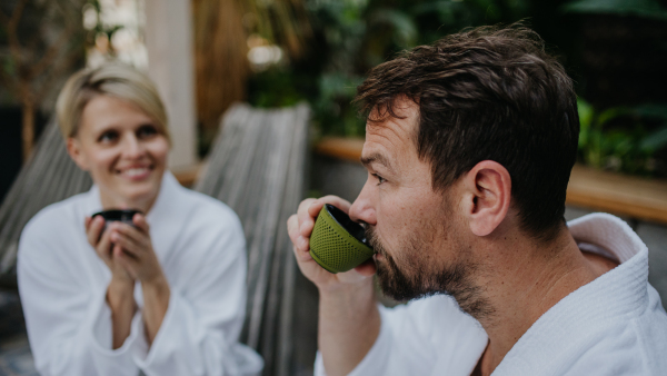 Couple in bathrobes drinking green tea, enjoying romantic wellness weekend in the spa. Concept of Valentine's Day.