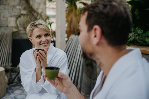 Couple in bathrobes drinking green tea, enjoying romantic wellness weekend in the spa. Concept of Valentine's Day.