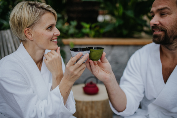 Couple in bathrobes drinking green tea, enjoying romantic wellness weekend in the spa. Concept of Valentine's Day.