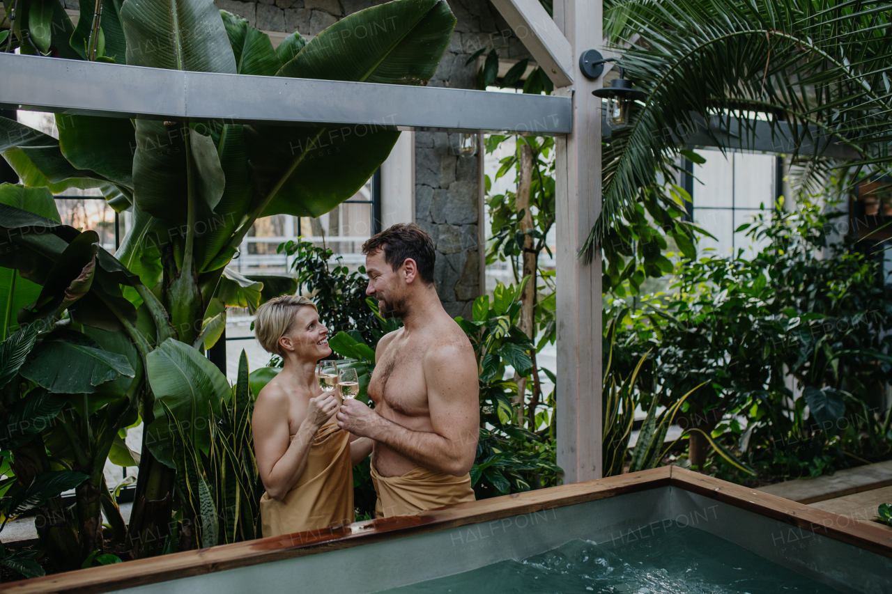 Beautiful couple standing hot tub, toasting and drinking champagne, enjoying romantic wellness weekend in spa. Concept of Valentine's Day.