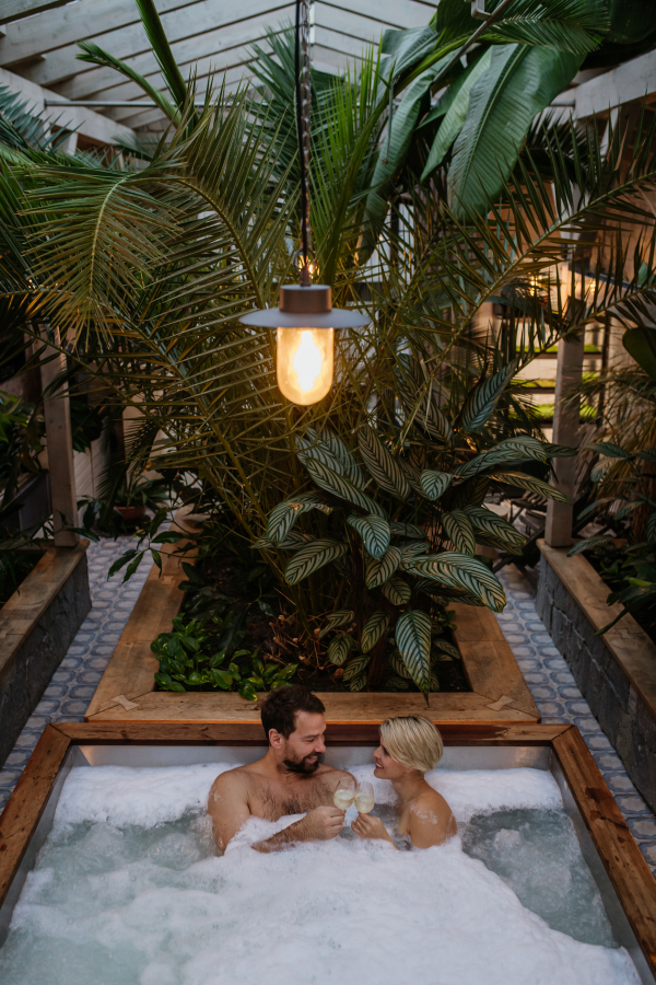 Beautiful mature couple relaxing in hot tub, drinking champagne, enjoying romantic wellness weekend in the spa. Concept of Valentine's Day.