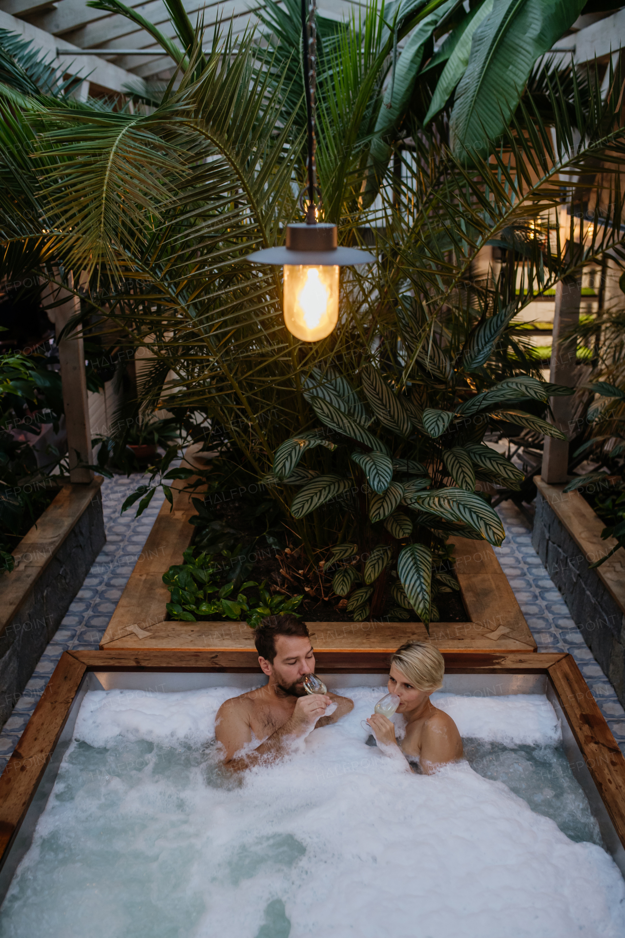 Beautiful mature couple relaxing in hot tub, drinking champagne, enjoying romantic wellness weekend in the spa. Concept of Valentine's Day.