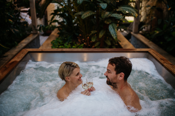 Beautiful mature couple relaxing in hot tub, drinking champagne, enjoying romantic wellness weekend in the spa. Concept of Valentine's Day.