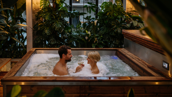 Beautiful mature couple relaxing in hot tub, drinking champagne, enjoying romantic wellness weekend in the spa. Concept of Valentine's Day.