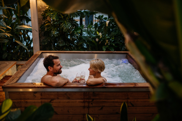 Beautiful mature couple relaxing in hot tub, drinking champagne, enjoying romantic wellness weekend in the spa. Concept of Valentine's Day.