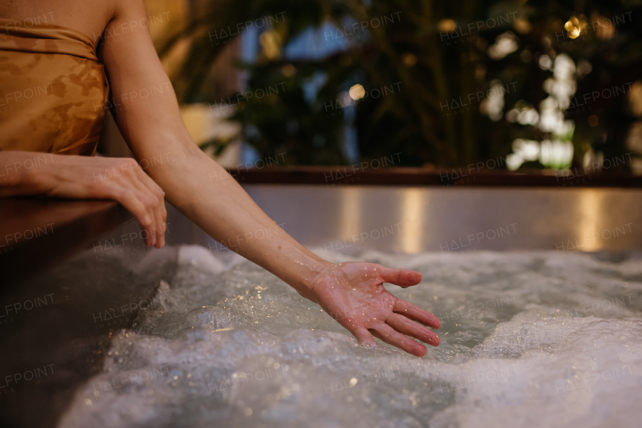 Close up of woman standing by hot tub, splashing water, enjoying wellness weekend in the spa.