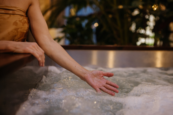 Close up of woman standing by hot tub, splashing water, enjoying wellness weekend in the spa.