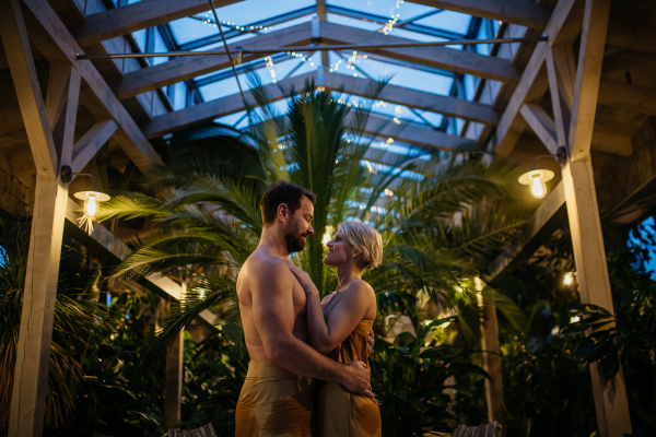 Beautiful couple standing in hotel greenhouse, looking at each another, enjoying romantic wellness weekend in the spa. Concept of Valentine's Day.