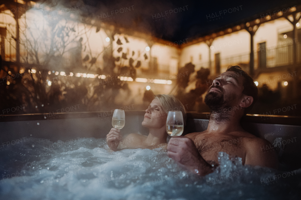 Beautiful mature couple relaxing in outdoor hot tub, drinking champagne, enjoying romantic wellness weekend in the spa. Concept of Valentine's Day.