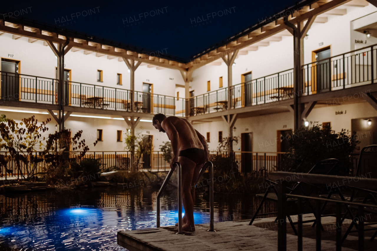 Mature man swimming in outdoor pool at night, enjoying calmness and empty pool. Wellness weekend in the hotel.