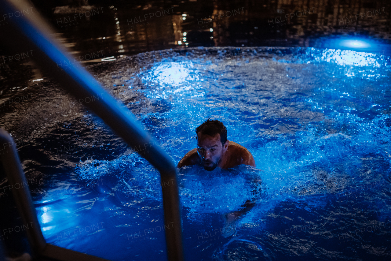 Mature man getting out of outdoor pool at night, enjoying calmness and empty pool. Wellness weekend in the hotel.