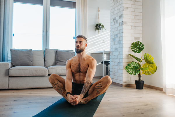 Handsome man doing yoga, stretching, resting after home workout, New Year's resolutions, exercising as healthy lifestyle and selfcare. Concept of morning or evening workout routine.