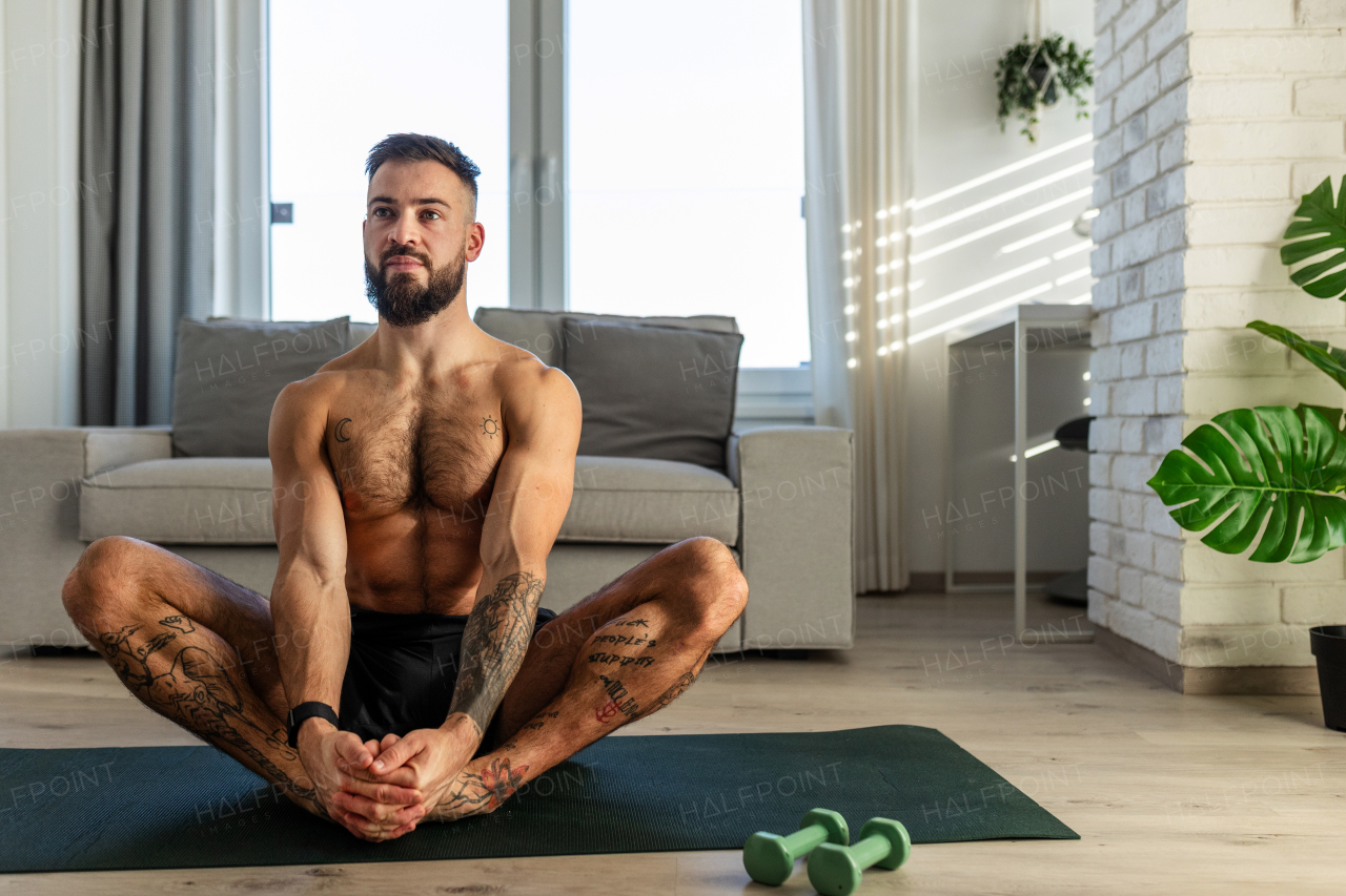 Handsome man doing yoga, stretching, resting after home workout, New Year's resolutions, exercising as healthy lifestyle and selfcare. Concept of morning or evening workout routine.