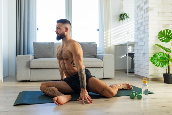 Handsome man doing yoga, stretching, resting after home workout, New Year's resolutions, exercising as healthy lifestyle and selfcare. Concept of morning or evening workout routine.