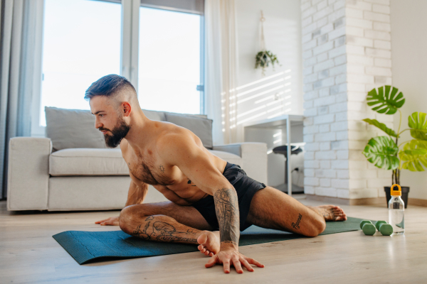 Handsome man doing yoga, stretching, resting after home workout, New Year's resolutions, exercising as healthy lifestyle and selfcare. Concept of morning or evening workout routine.