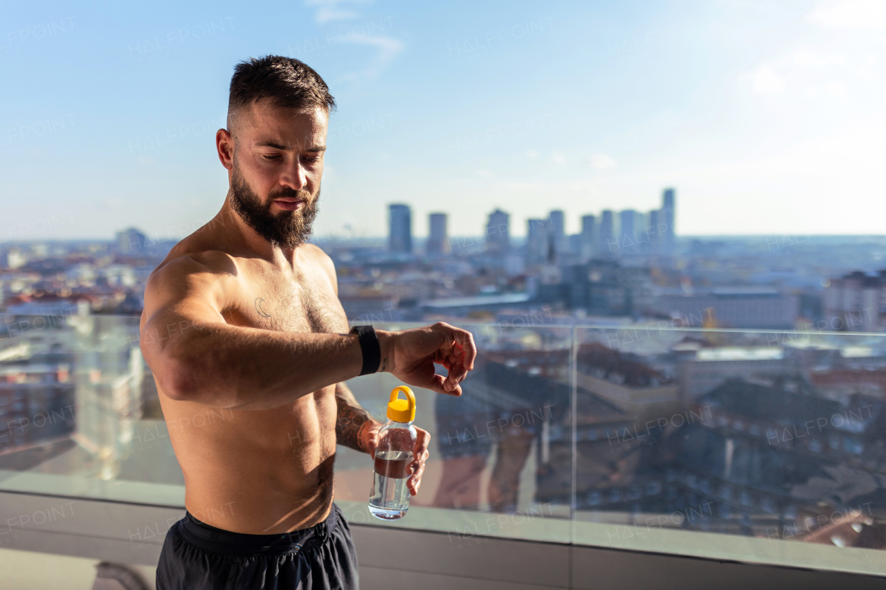 Man after home workout, checking his exercise performance on smartwatch, standing on balcony. Morning or evening workout routine.