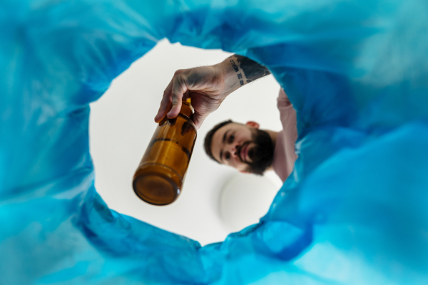 Man throwing glass bottle into recycling bin. Throwing empty alcohol bottle, New Year's resolutions, drink less alcohol healthy lifestyle without alcoholic drinks.