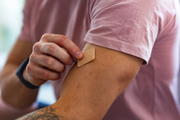 Young man putting nicotine patch on his shoulder, New Year's resolutions, quitting smoking and healthy lifestyle without cigarettes.