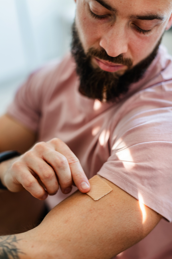 Young man putting nicotine patch on his shoulder, New Year's resolutions, quitting smoking and healthy lifestyle without cigarettes.