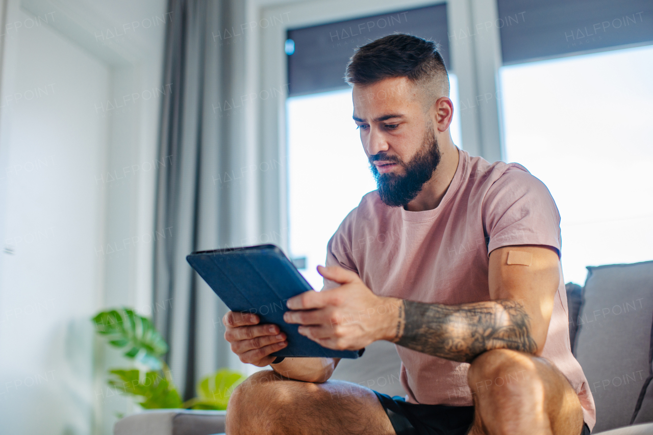 Young man with nicotine patch on his shoulder, holding tablet. New Year's resolutions, quitting smoking and healthy lifestyle without cigarettes.