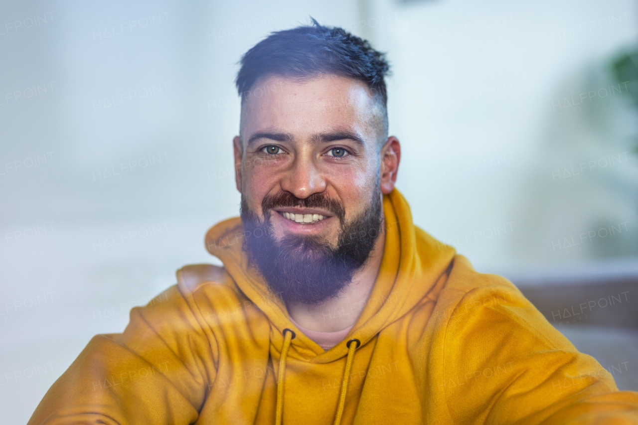 Calm man in yellow sweatshirt looking at camera and smiling.