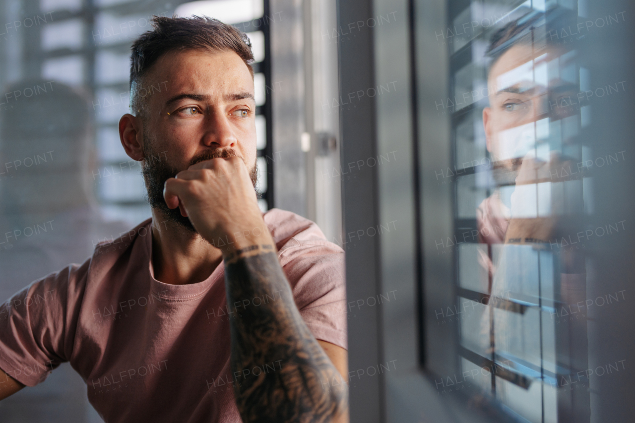 Handsome calm man in pink t-shirt with tattoo on arms looking through window.