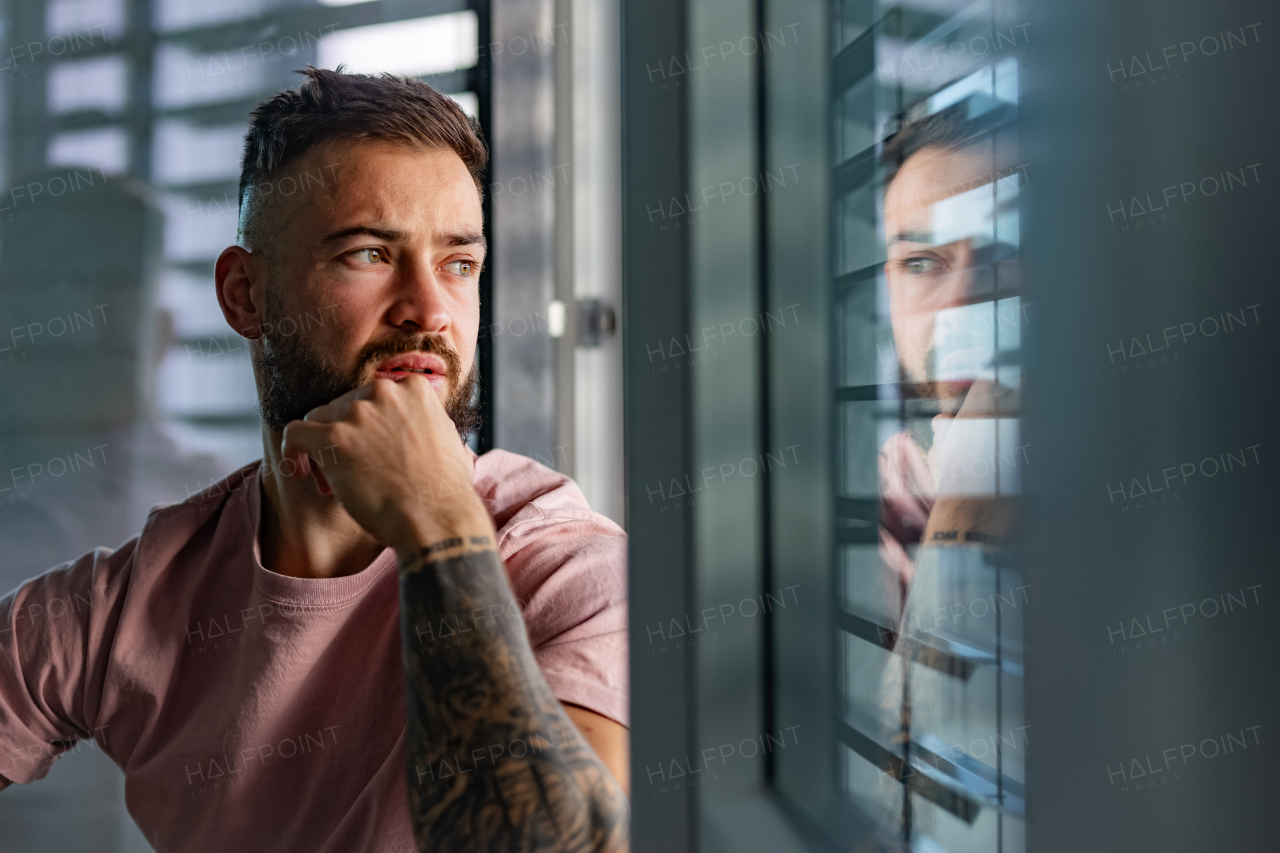 Handsome calm man in pink t-shirt with tattoo on arms looking through window.