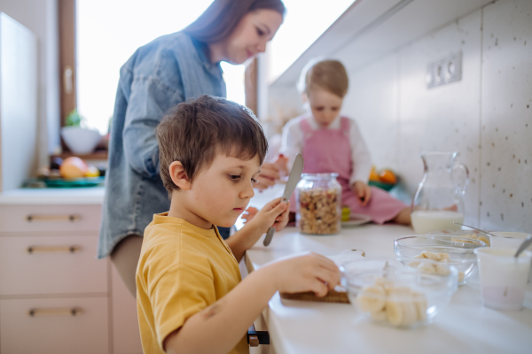 A mother of two little children preparing breakfast in kitchen at home.