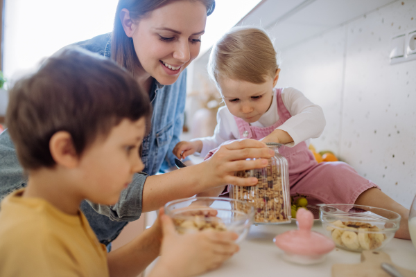 A mother of two little children preparing breakfast in kitchen at home.