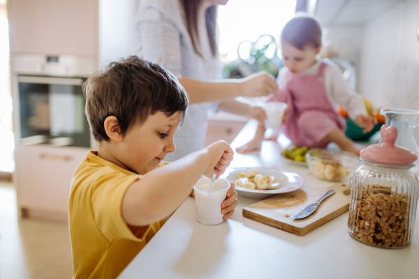 A mother of two little children preparing breakfast in kitchen at home.