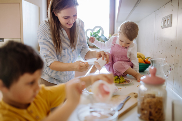 A mother of two little children preparing breakfast in kitchen at home.