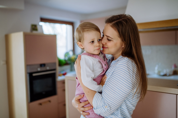 A young mother hugging her little daughter at home, lifting her up.