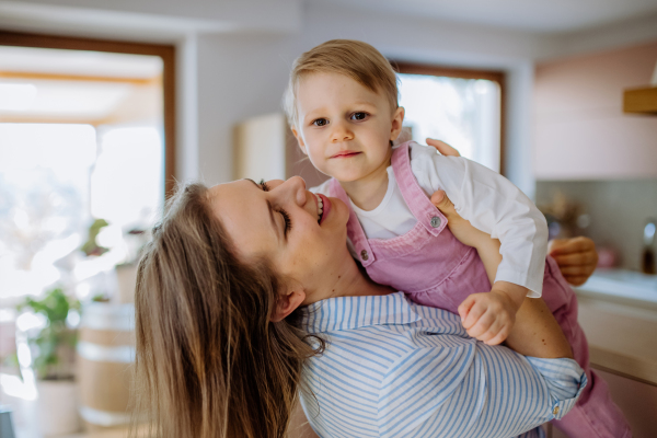 A young mother hugging her little daughter at home, lifting her up.