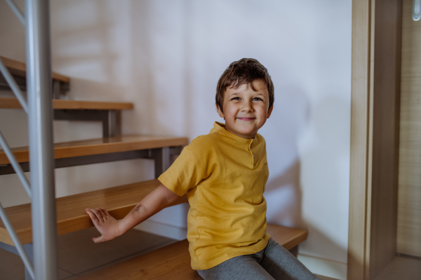 A cute little boy sitting on stairs at home.