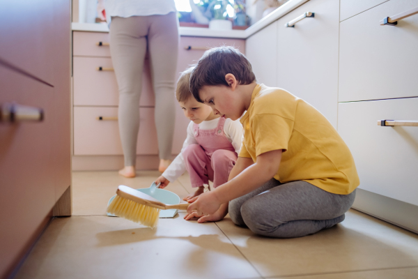 A little boy and girl helping to clean house using pan and brush as they sweep up dirt off floor.