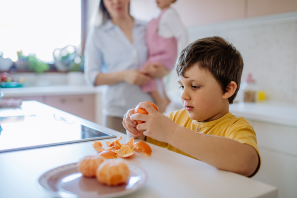 Little boy peeling a tangerine for him and his little sister. Mother in background.